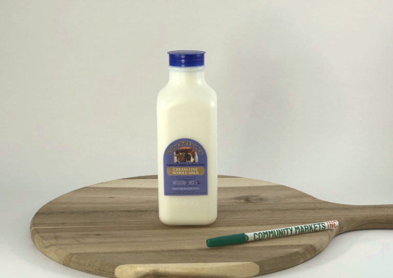 A 1-pint container of Creamline Milk from Walnut Hill Farm sitting on a cutting board and next to a standard ballpoint pen for scale.